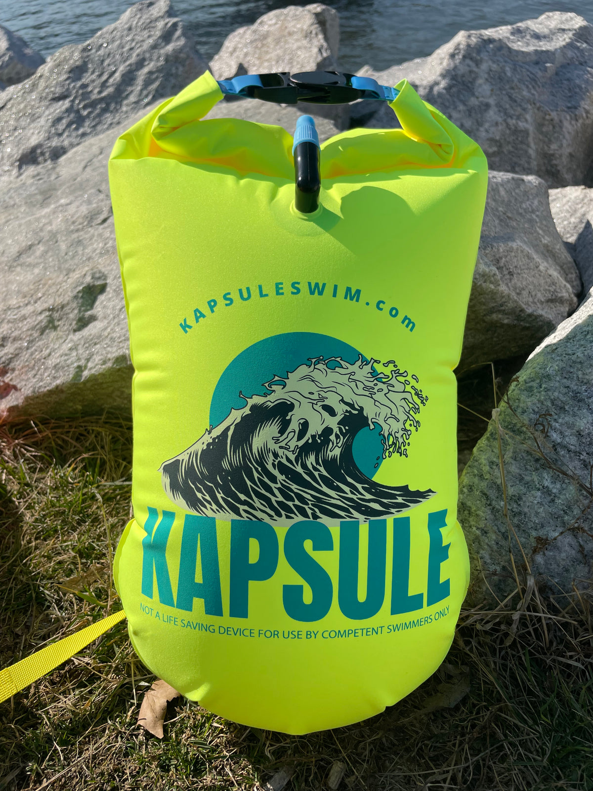 KAPSULE Atlas swim buoy 20L neon yellow open water safety float on rocky shoreline